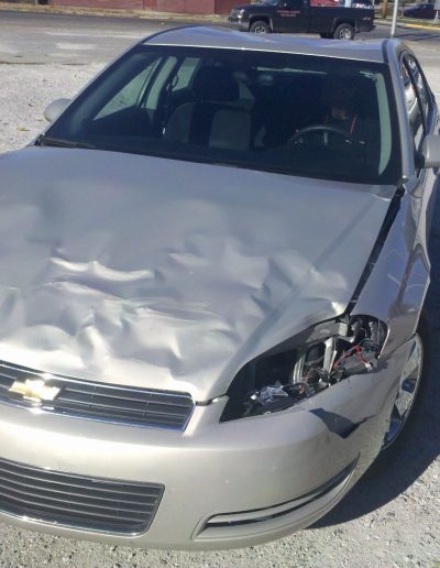 A silver Chevy car with a damaged hood and headlights